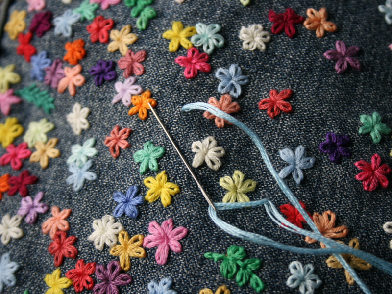 An example of hand embroidery on denim covered in colourful flowers.